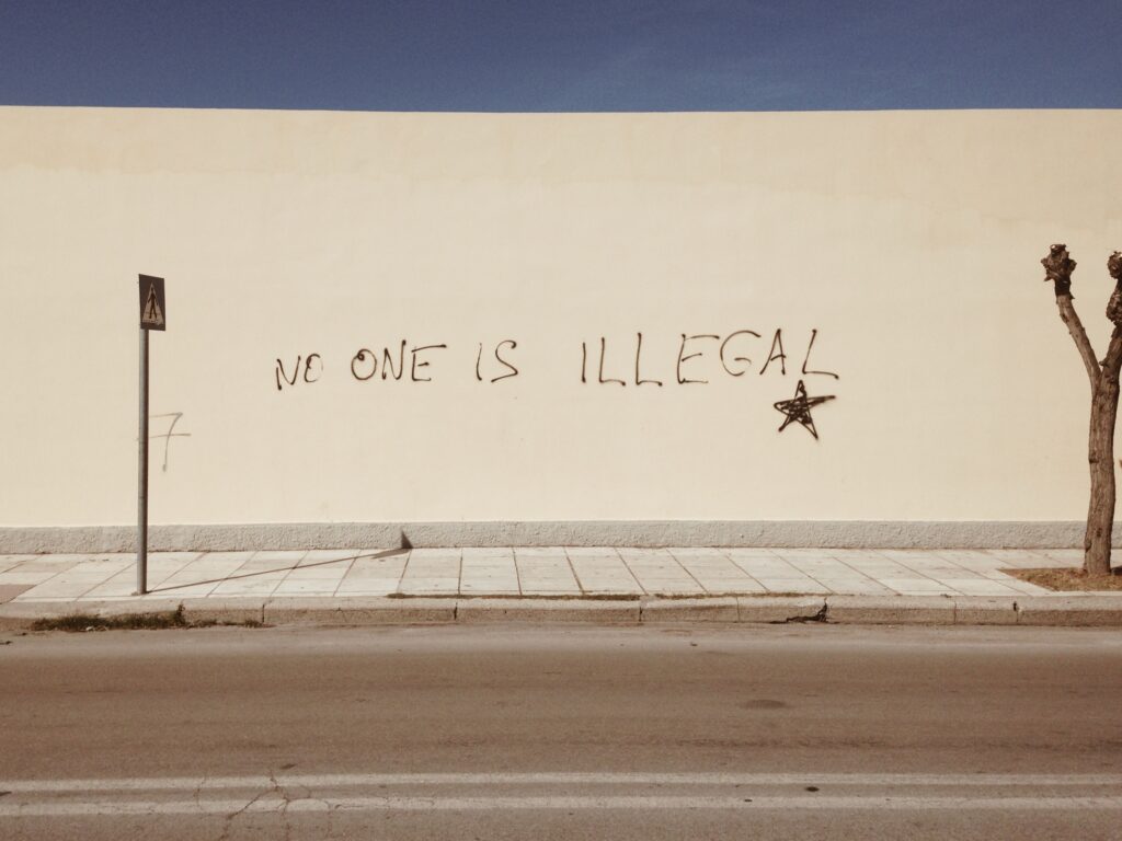 Photo of white wall with grafitti text: No one is illegal